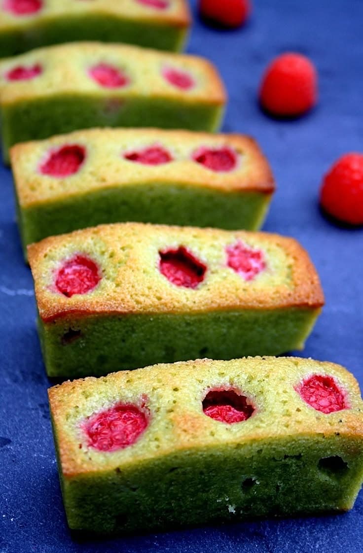 Financiers au matcha garnis de framboises alignés sur un fond bleu